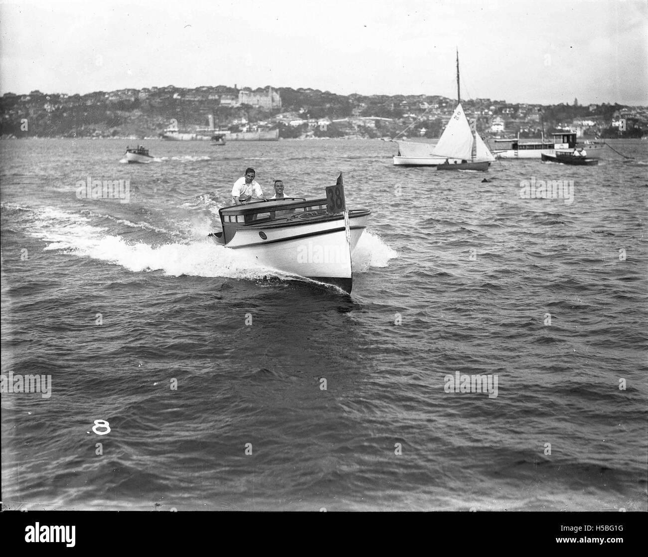 Un motoscafo è visto sul porto di Sydney con due uomini a bordo. Questa immagine mette in evidenza l'uso ricreativo del porto, un luogo popolare per la nautica da diporto e gli sport acquatici in Australia. Foto Stock