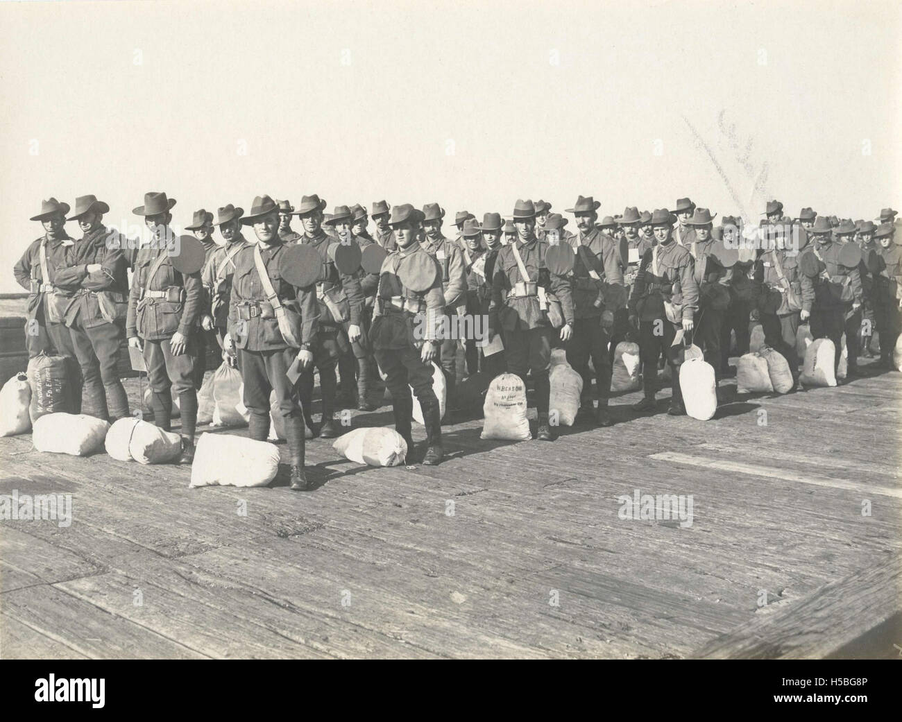 Una fotografia di soldati in fila e in attesa di salire a bordo della nave truppe WARILDA. L'immagine cattura un momento di preparazione militare mentre i soldati si preparano per lo spiegamento, riflettendo il significato storico delle navi da guerra. Foto Stock