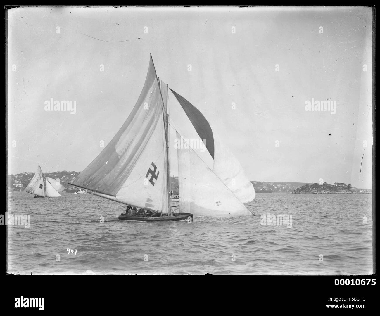 Uno yacht è raffigurato sotto la barca a vela nel porto di Sydney, con un emblema di svastica visibile. L'immagine probabilmente cattura un momento storico, forse legato alle attività navali pre-seconda guerra mondiale o a un evento specifico che coinvolge lo yacht. Foto Stock