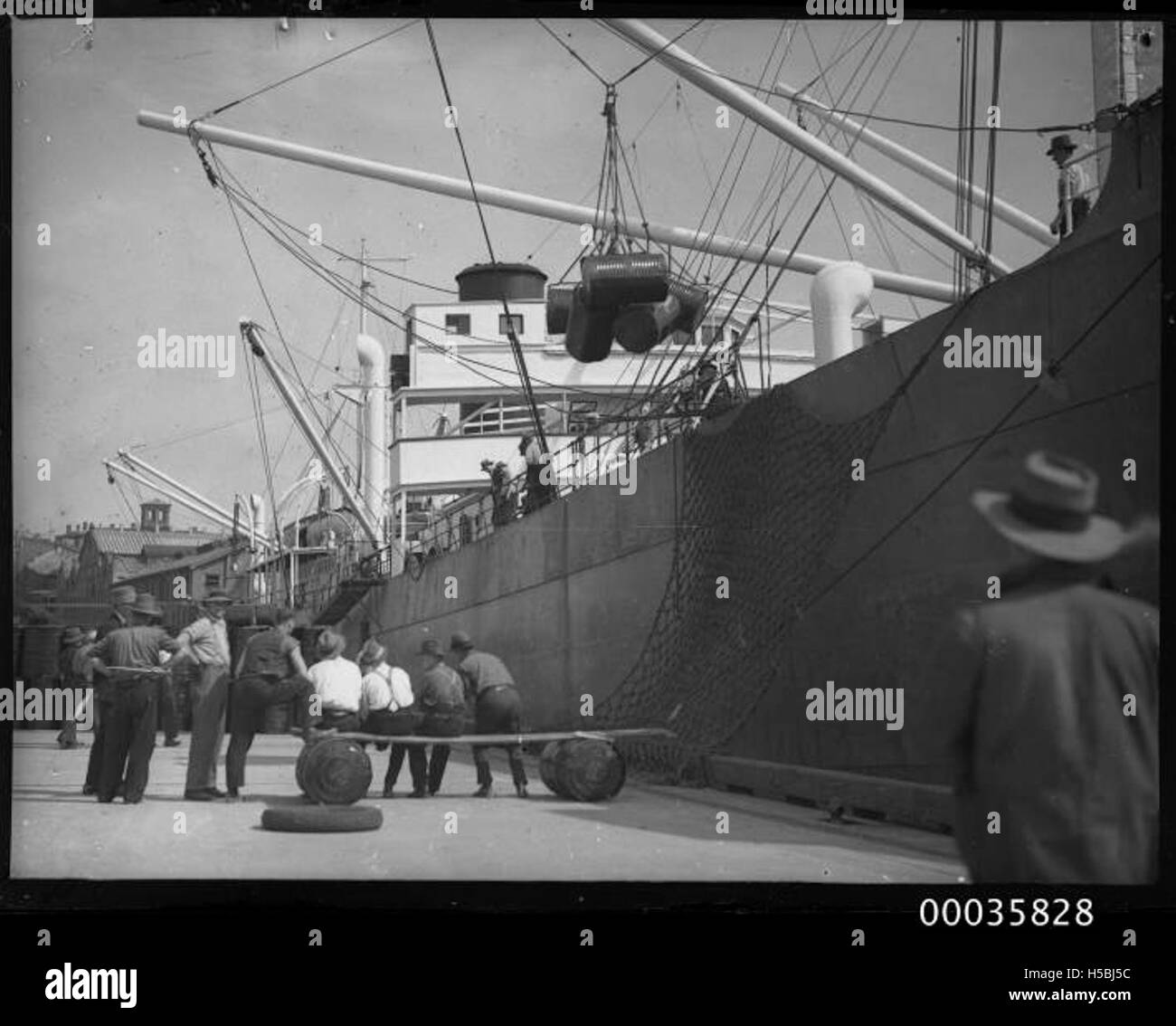 La MV Neptunian è ormeggiata a Johnstons Bay a Sydney, dove gli operai scaricano fusti d'olio per H C Sleigh. L'immagine riflette il commercio marittimo e le attività industriali che facevano parte delle operazioni portuali di Sydney. Foto Stock