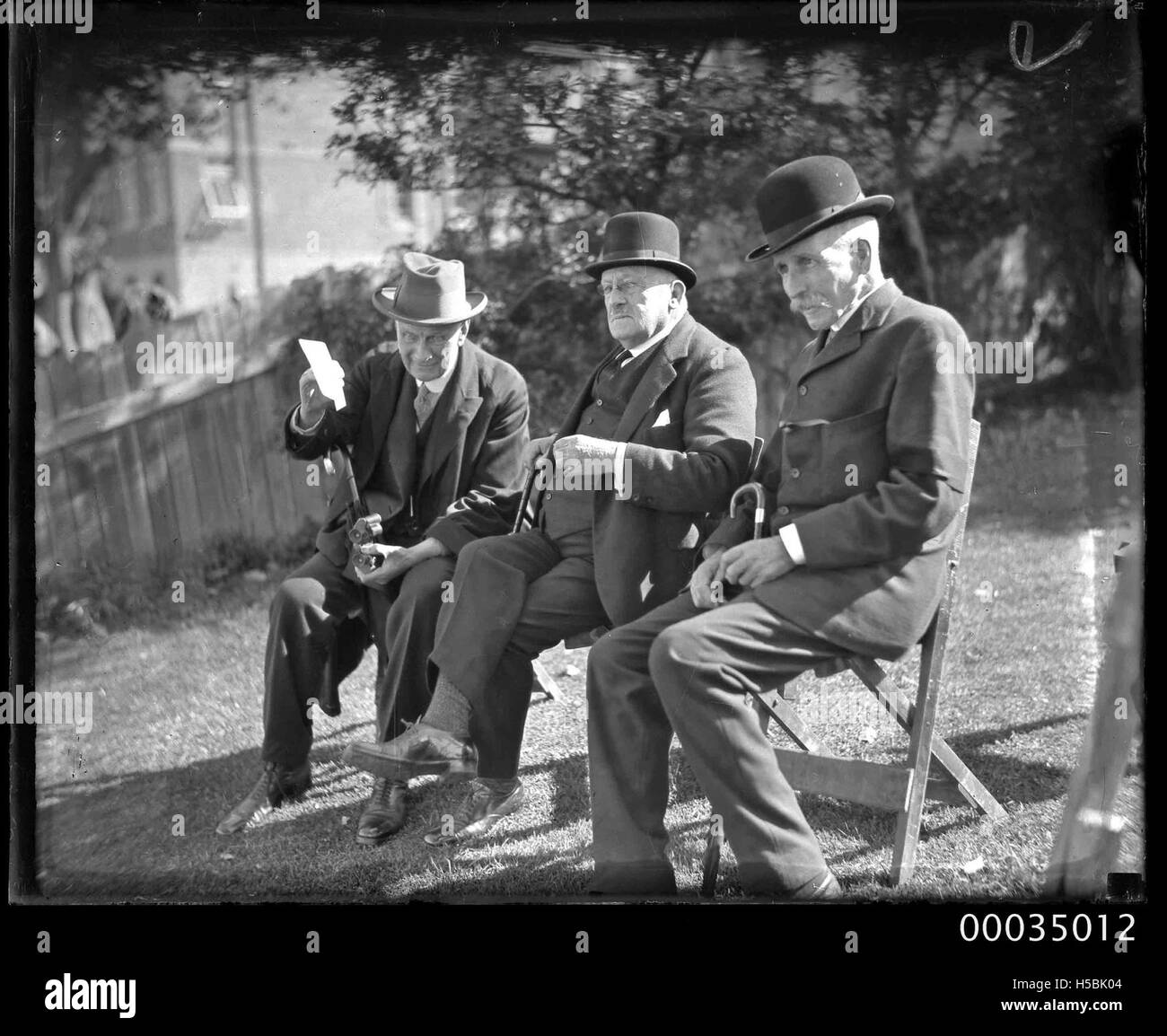 Tre uomini, ivi compreso il giudice Alfred Paxton Backhouse, indossando abiti e cappelli seduto su un prato, 1910-1939 Foto Stock