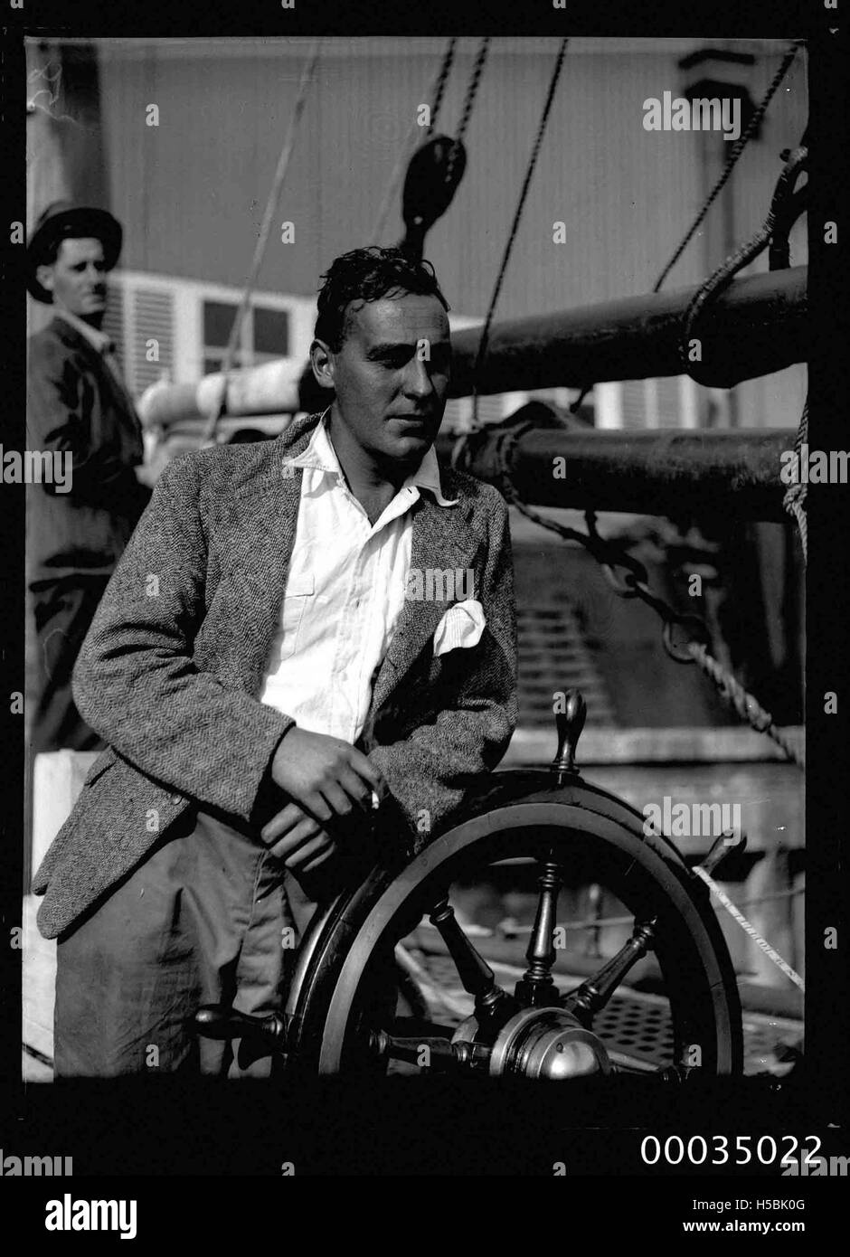 Un uomo è visto al volante del ketch a vela CORWA, parte della COLLEZIONE HOOD. Questa immagine evidenzia il ruolo del capitano o dell'equipaggio nella gestione della nave durante il viaggio. Foto Stock