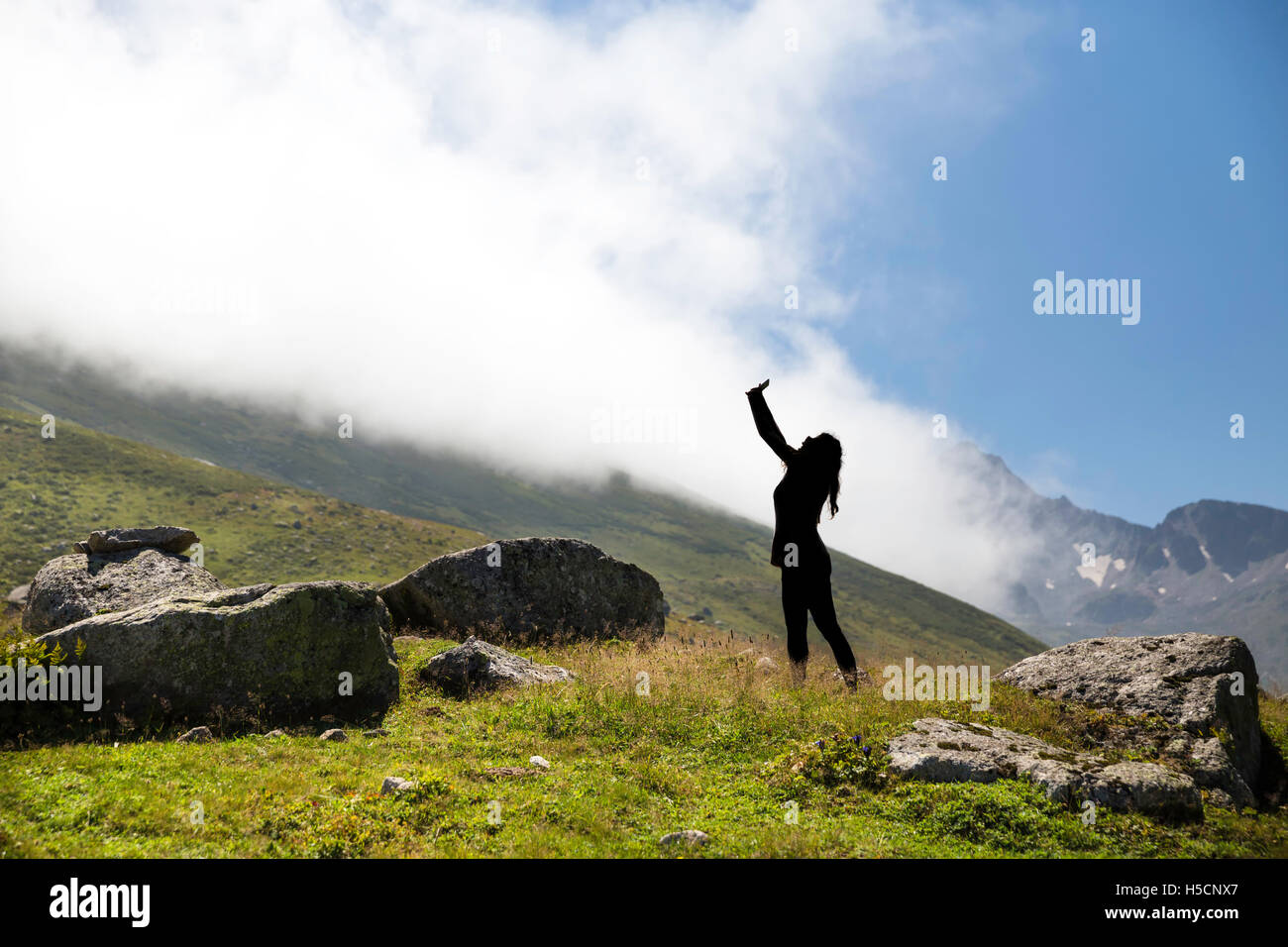 Unico irriconoscibile silhouette di donna prendendo un selfie sulla cima della montagna con sfondo velato Foto Stock