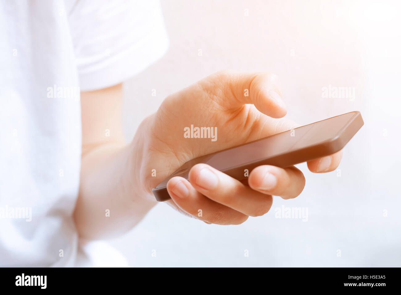 Utilizza lo smartphone con una sola mano in interni luminosi al tramonto Foto Stock
