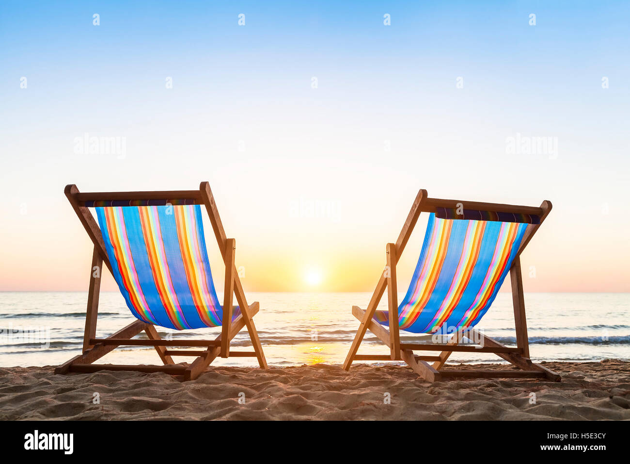 Due sedie a sdraio su una spiaggia sabbiosa tropicale con un bellissimo tramonto colorato Foto Stock