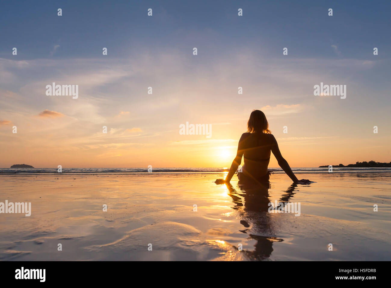 Ragazza bionda in vacanza rilassante sulla spiaggia e guardando il tramonto Foto Stock
