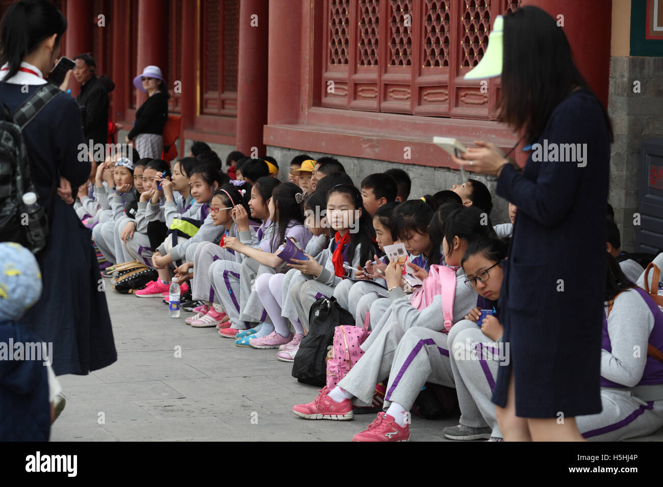 I bambini cinesi, alunni, indossano uniformi scolastiche, sedersi sul terreno obbediente durante una gita del patrimonio con i loro insegnanti. Foto Stock