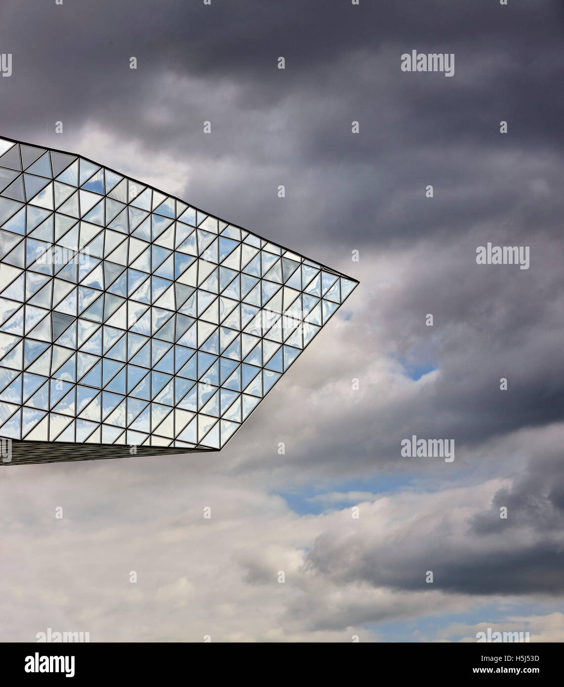 Opache e trasparenti le sfaccettature di vetro contro il cielo in tempesta. Casa porta ad Anversa, Belgio. Architetto: Zaha Hadid Architects, 2016. Foto Stock