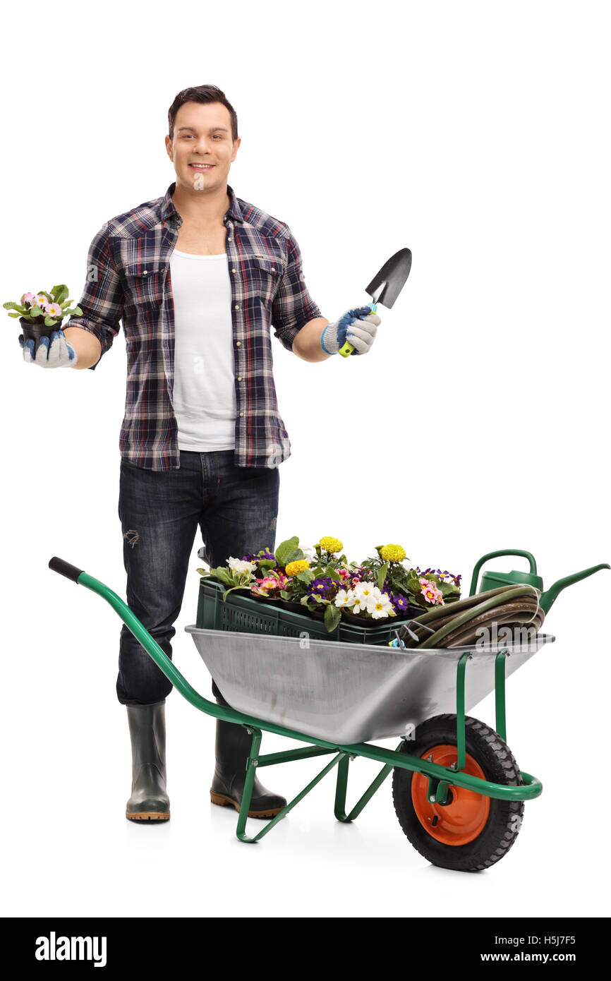 Giardiniere maschio in piedi dietro una carriola e tenendo un fiore in un vaso e un capocorda isolato su sfondo bianco Foto Stock