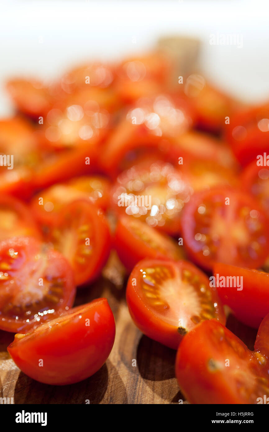 Rossi pomodori ciliegini tagliati a metà sul tagliere Foto Stock