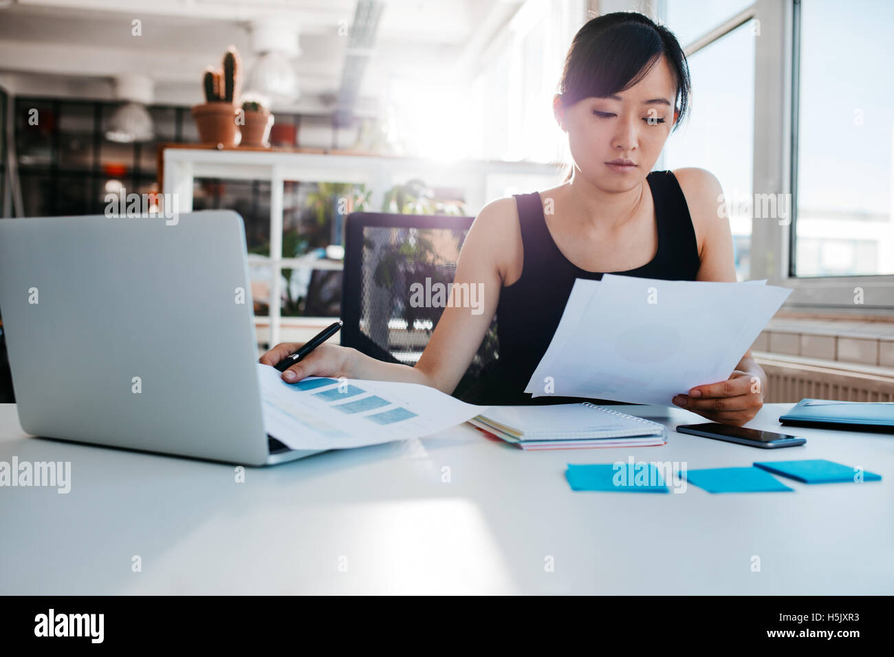 Ritratto di giovane donna asiatica la lettura dei documenti alla sua scrivania. Imprenditrice al suo posto di lavoro facendo i documenti. Foto Stock