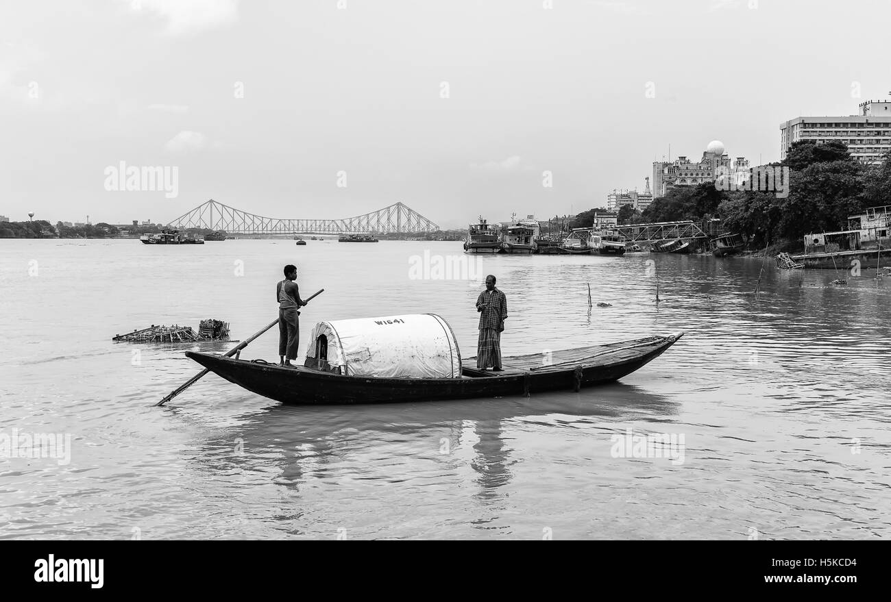 Due uomini attraversare il Fiume Hooghly nella piccola imbarcazione in legno con vista della vecchia quella di Howrah bridge su una tranquilla mattina dopo piogge monsoniche. Foto Stock