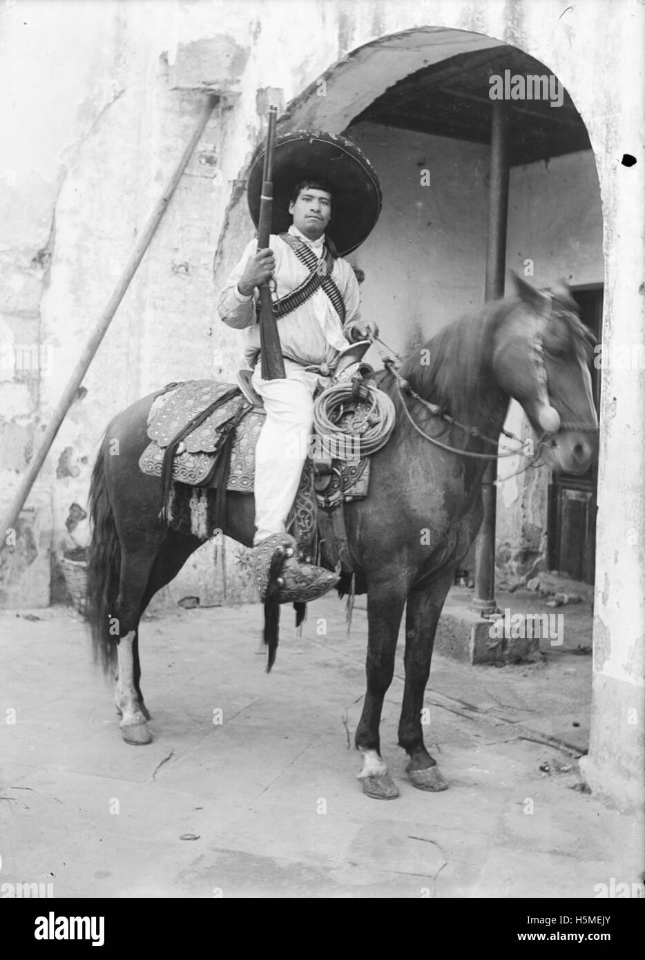 Questa immagine raffigura un soldato rivoluzionario armato a cavallo, probabilmente proveniente da un conflitto rivoluzionario. Il soldato è visto portare armi da fuoco, sottolineando il ruolo della cavalleria nelle battaglie storiche e nelle rivoluzioni. Foto Stock