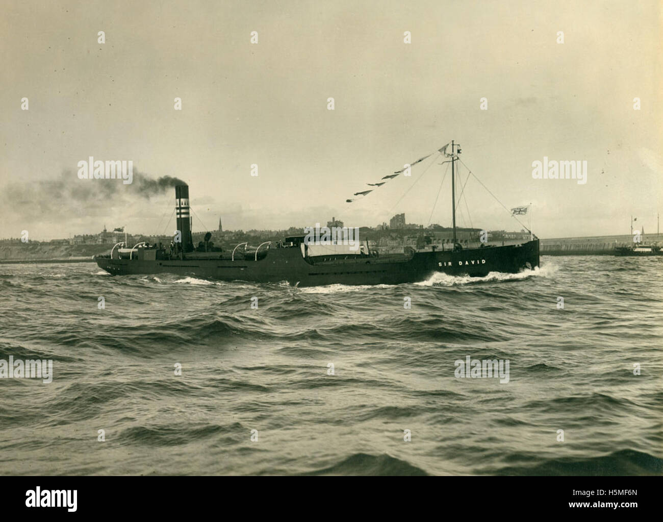 Questa fotografia in bianco e nero mostra la nave da carico "Sir David" che ha lasciato il fiume Tyne nel 1927. Costruita dai costruttori navali britannici per la Hain Steamship Company, la nave faceva parte dell'industria marittima di South Shields, Tyneside. L'immagine evidenzia la partenza della nave, con vedute del cantiere navale, delle strutture industriali e del fiume Tyne, che riflette il patrimonio della costruzione navale della regione. Foto Stock