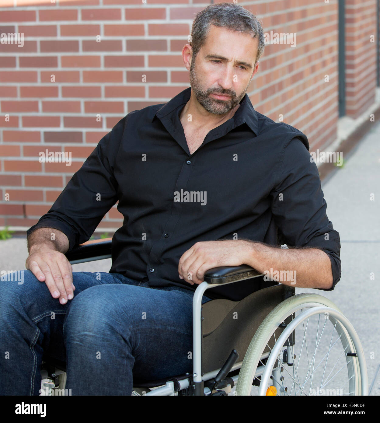Bel uomo seduto nella sedia a rotelle e cercando premuto Foto Stock