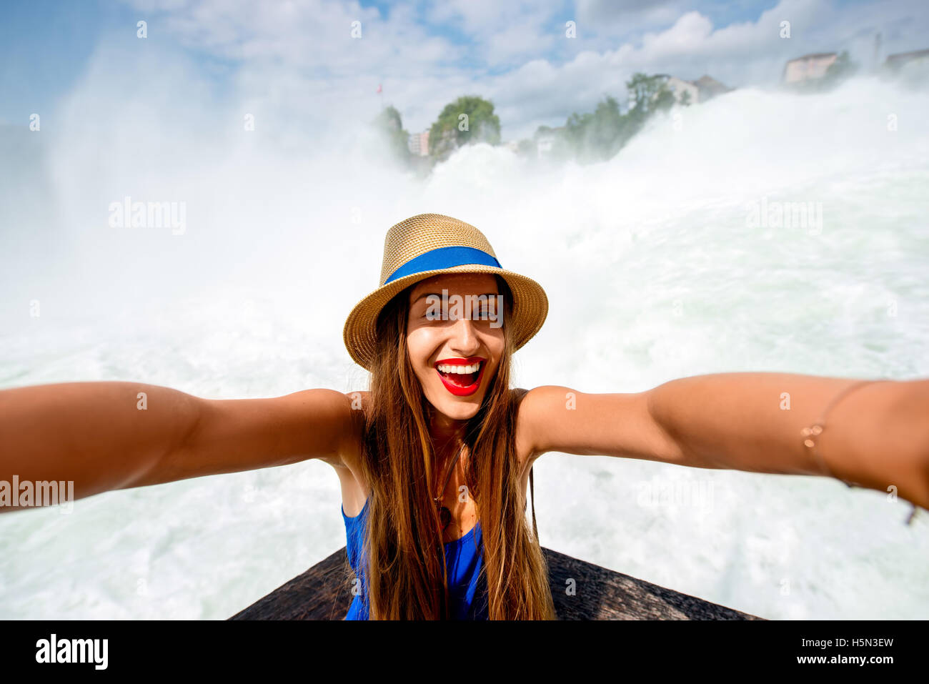 Emozionato turista femminile rendendo ritratto di auto di fronte alle famose cascate del Reno. Donna avente una grande vacanza in Svizzera Foto Stock