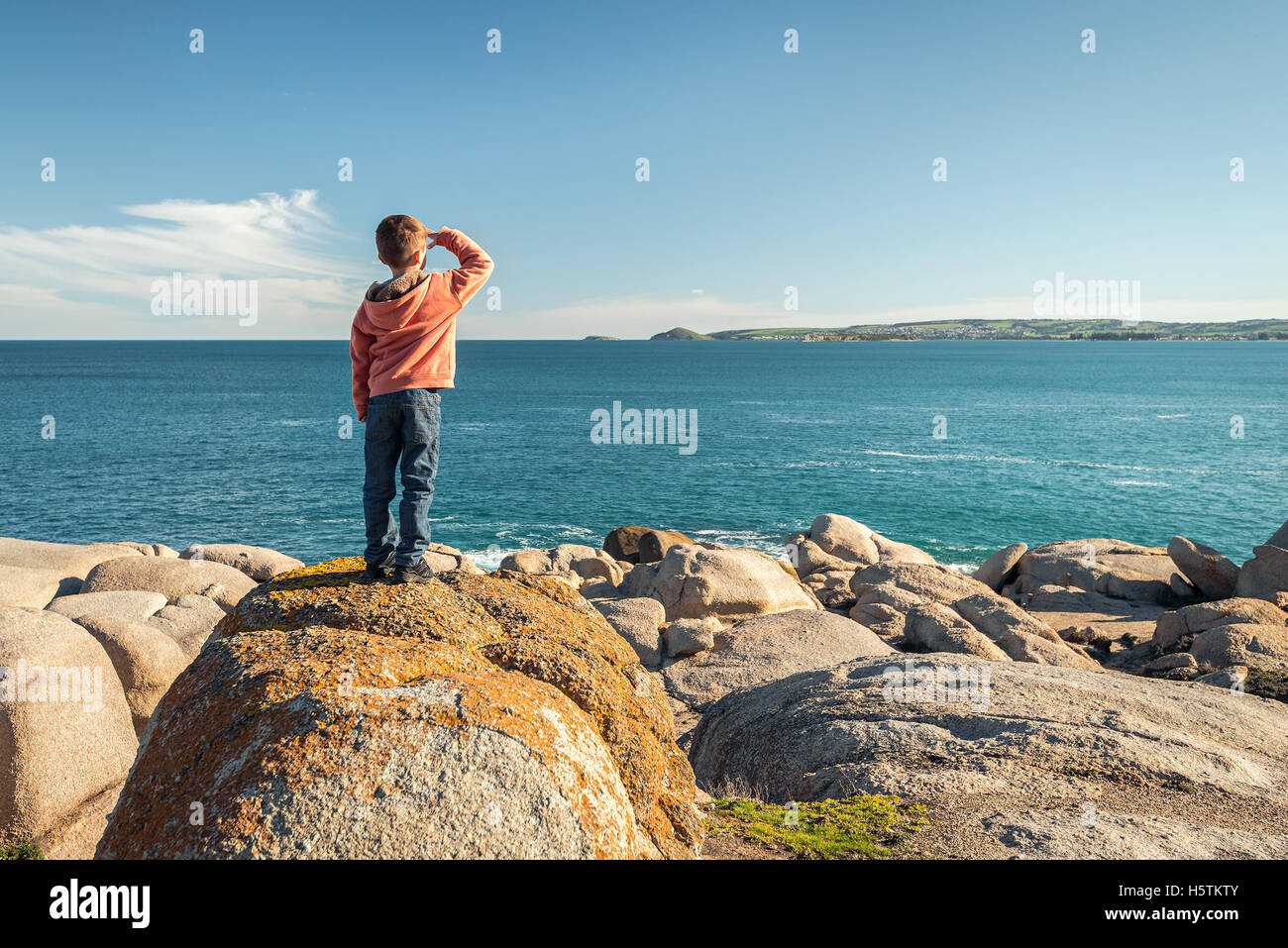 Ragazzo in piedi sul bordo della roccia e guardando verso il mare a Port Elliot, Sud Australia. Tonificazione del colore applicato Foto Stock