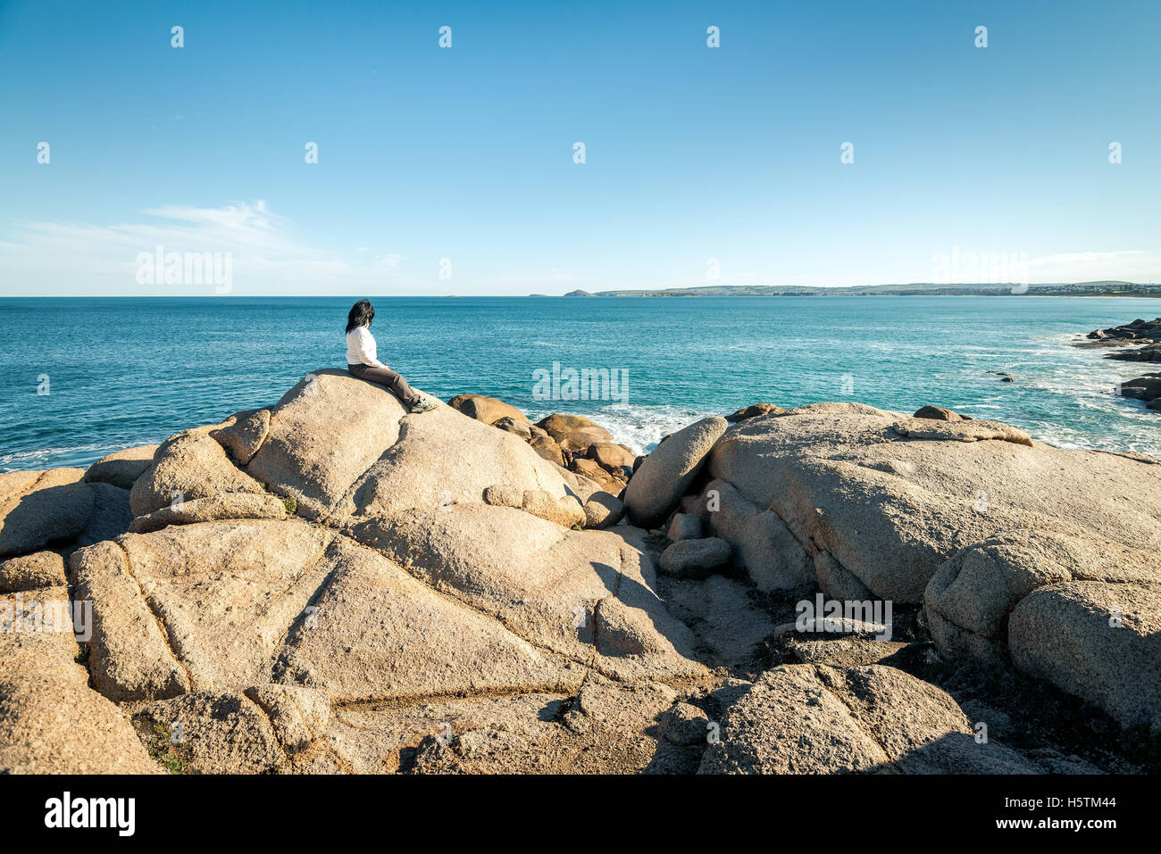 Donna seduta sul bordo della roccia e guardando verso il mare a Port Elliot, Sud Australia Foto Stock