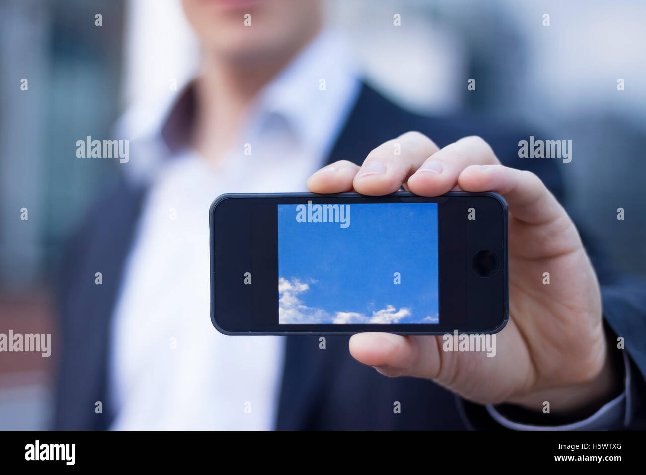 Imprenditore che mostra lo schermo dello smartphone con edifici per uffici in background Foto Stock