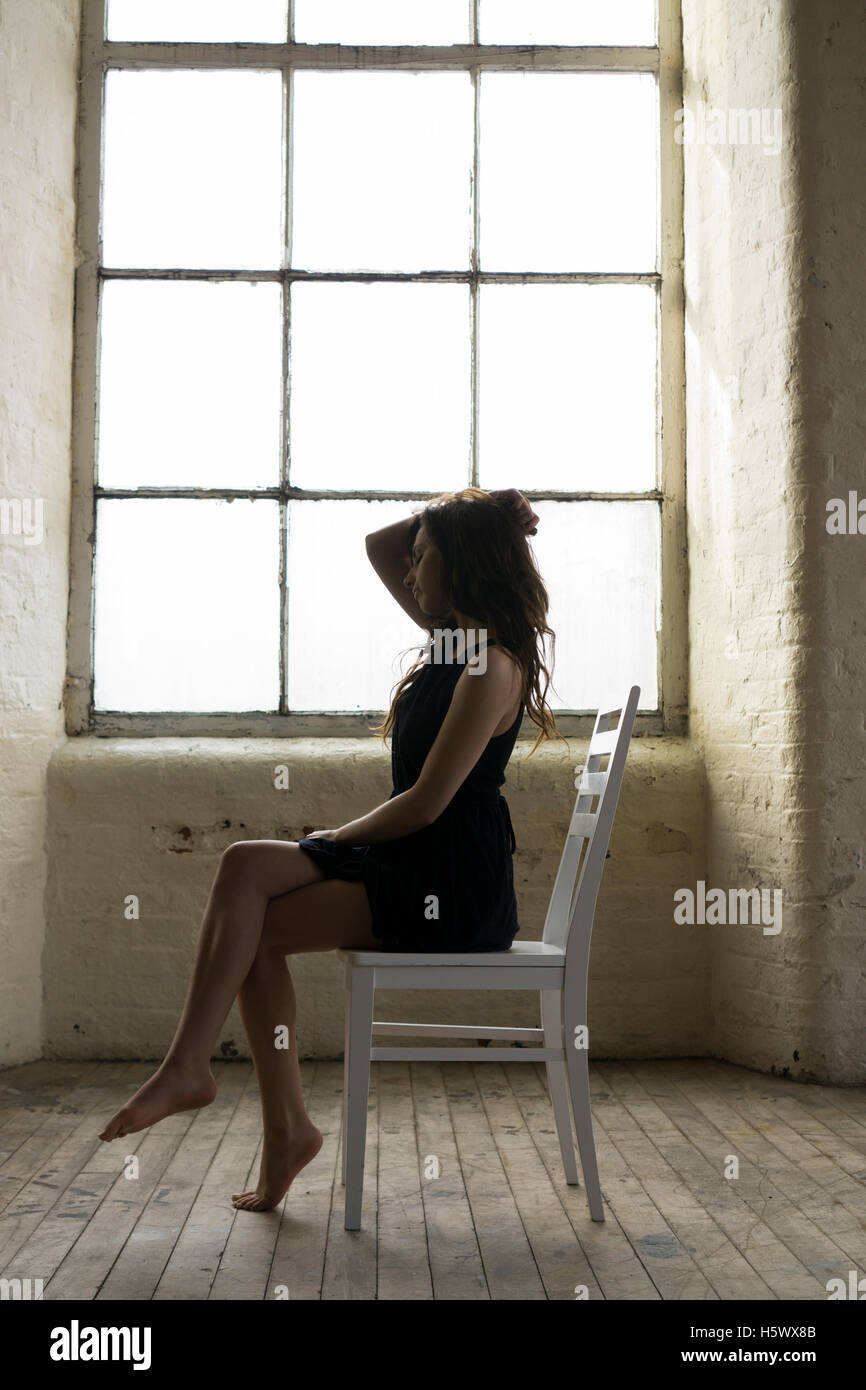 Triste donna seduta su una sedia da finestra Foto Stock