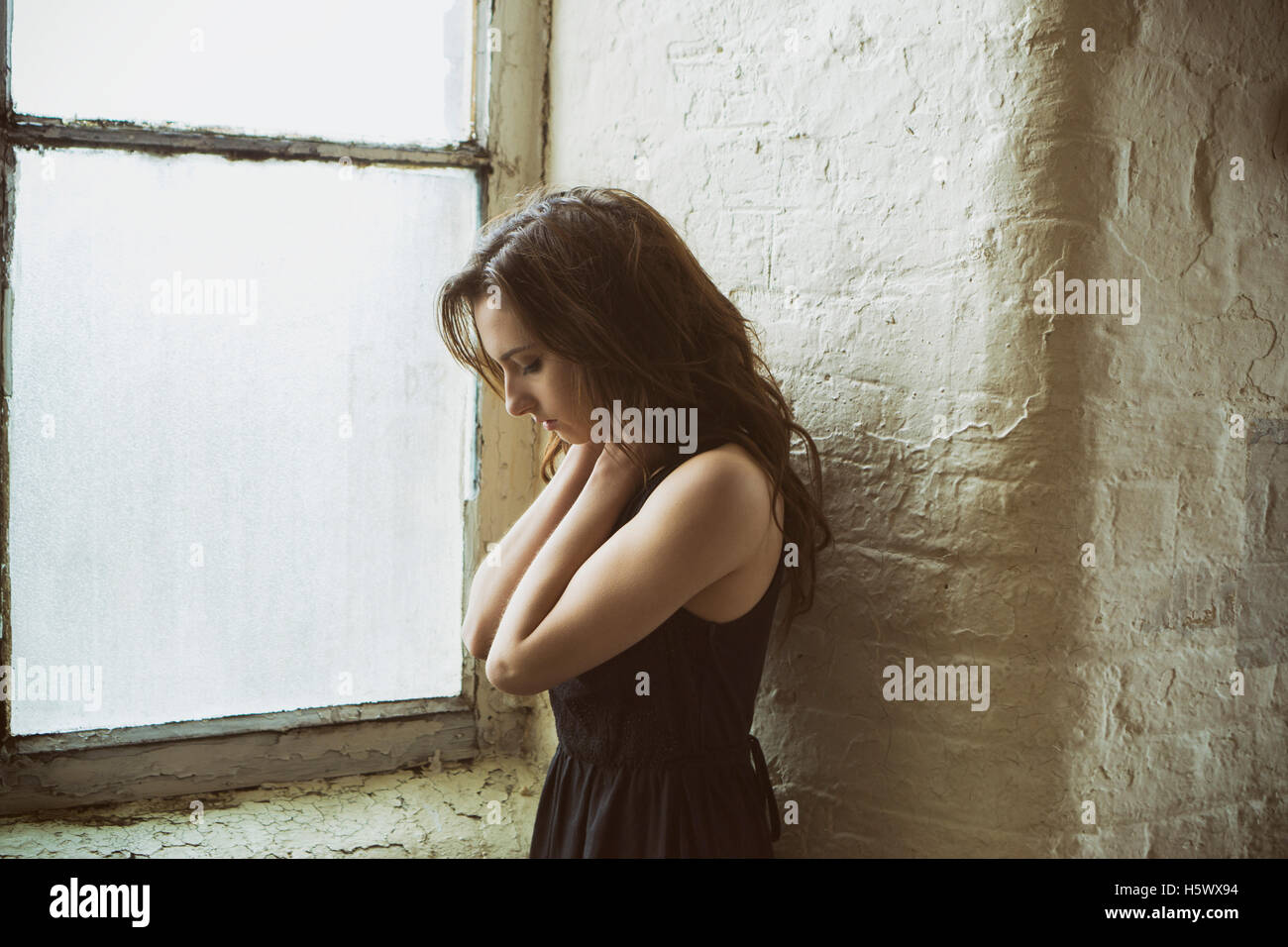 Triste giovane donna in piedi vicino alla finestra le mani sul collo Foto Stock