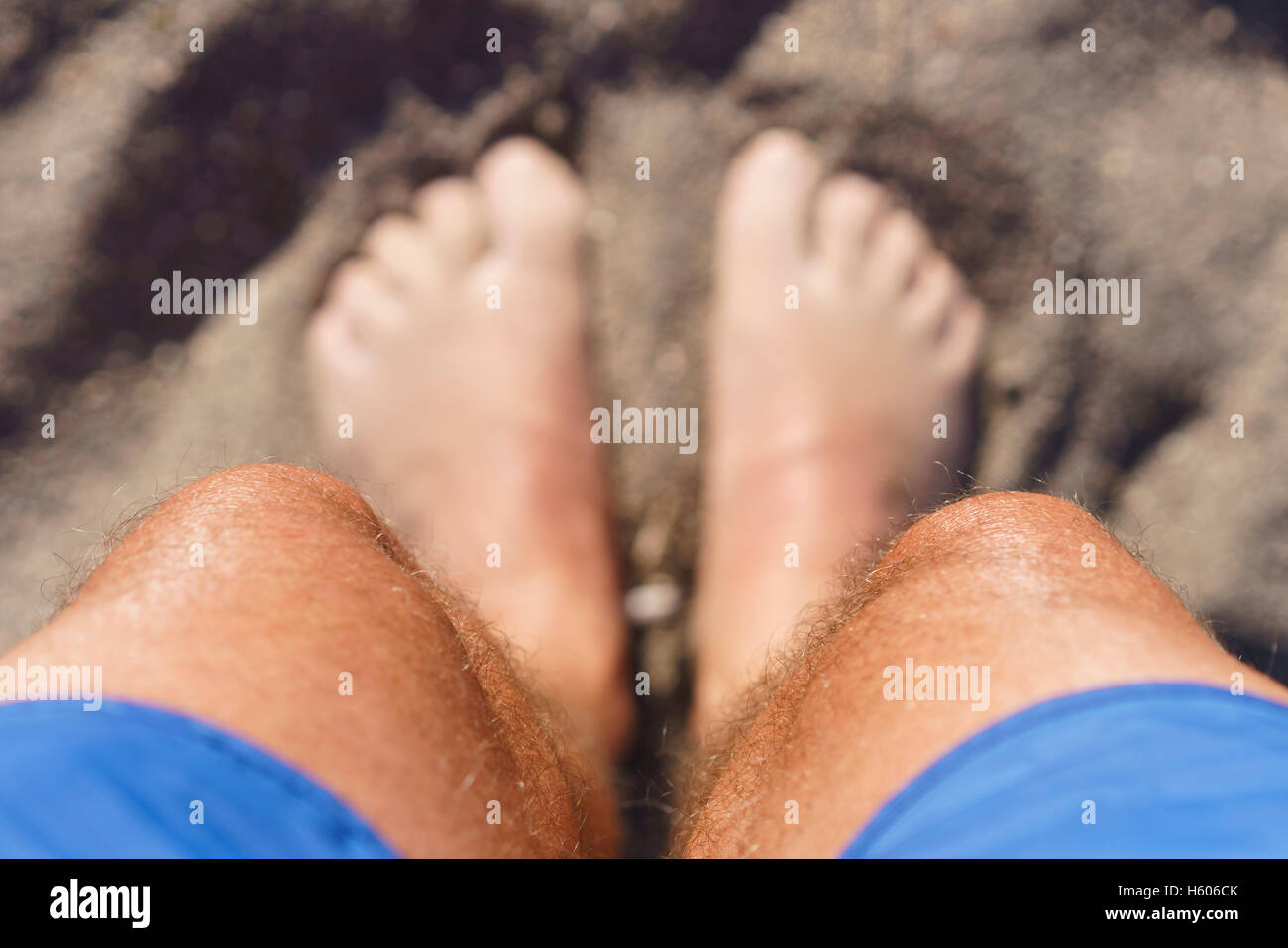 Guardando in giù ai miei piedi sulla spiaggia mentre con le dita dei piedi nella sabbia Foto Stock
