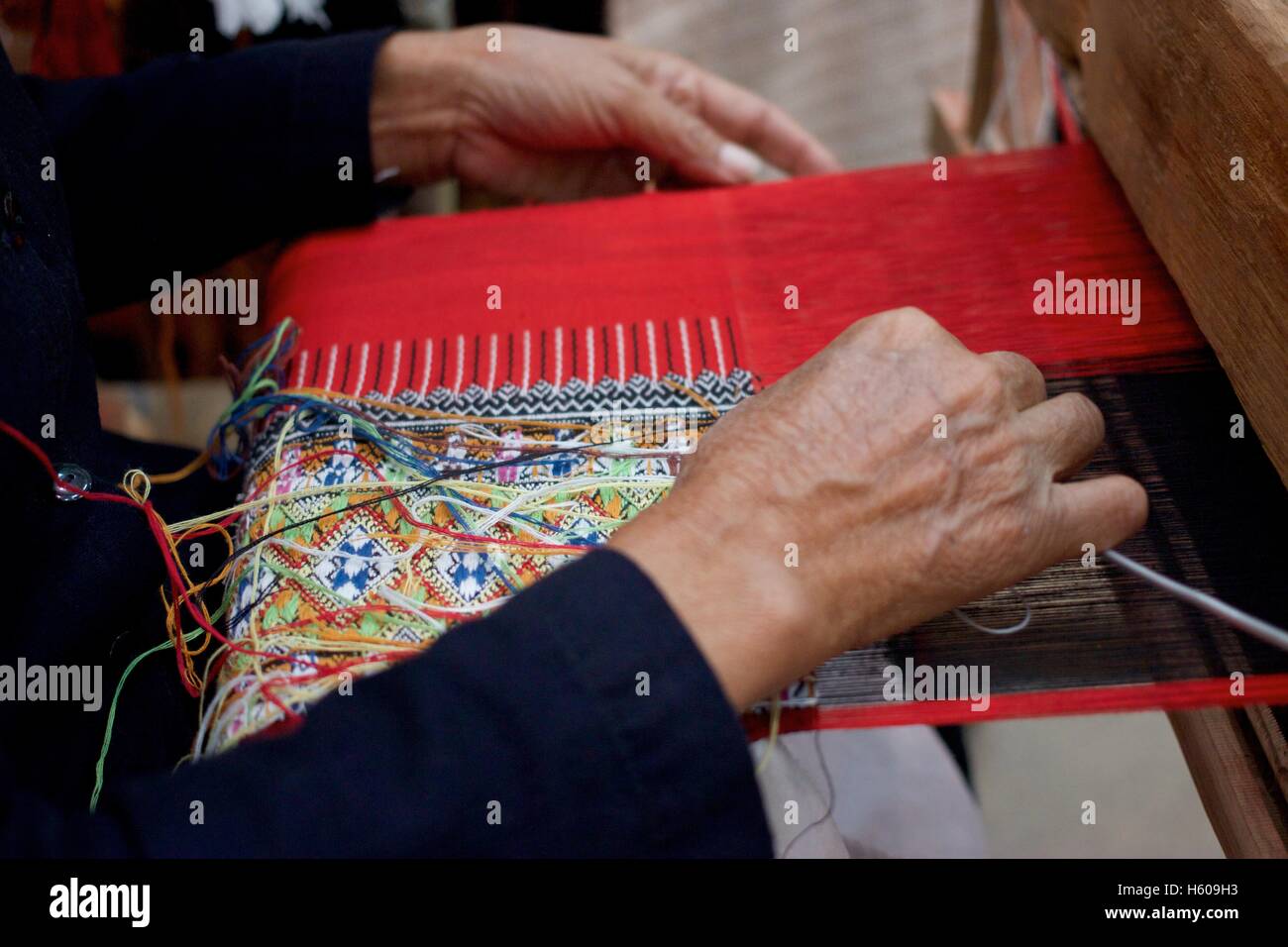 Donna vecchia tessitura di rosso e nero multi colore bandiera di cotone modello sul telaio nel nord della Thailandia Foto Stock