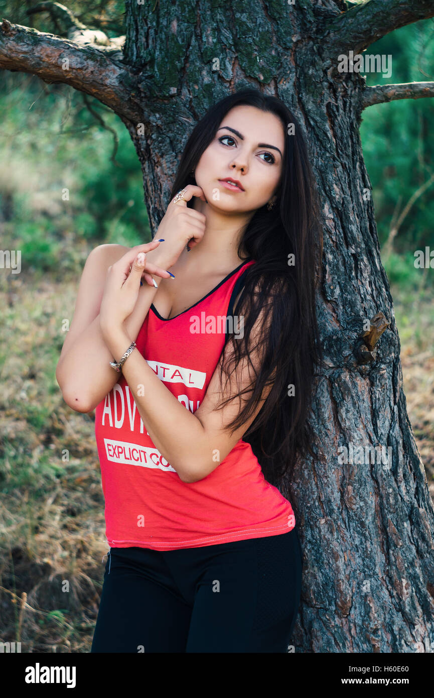 Giovane bella bruna modello in posa l'immagine sportiva del parco contro lo sfondo di alberi Foto Stock