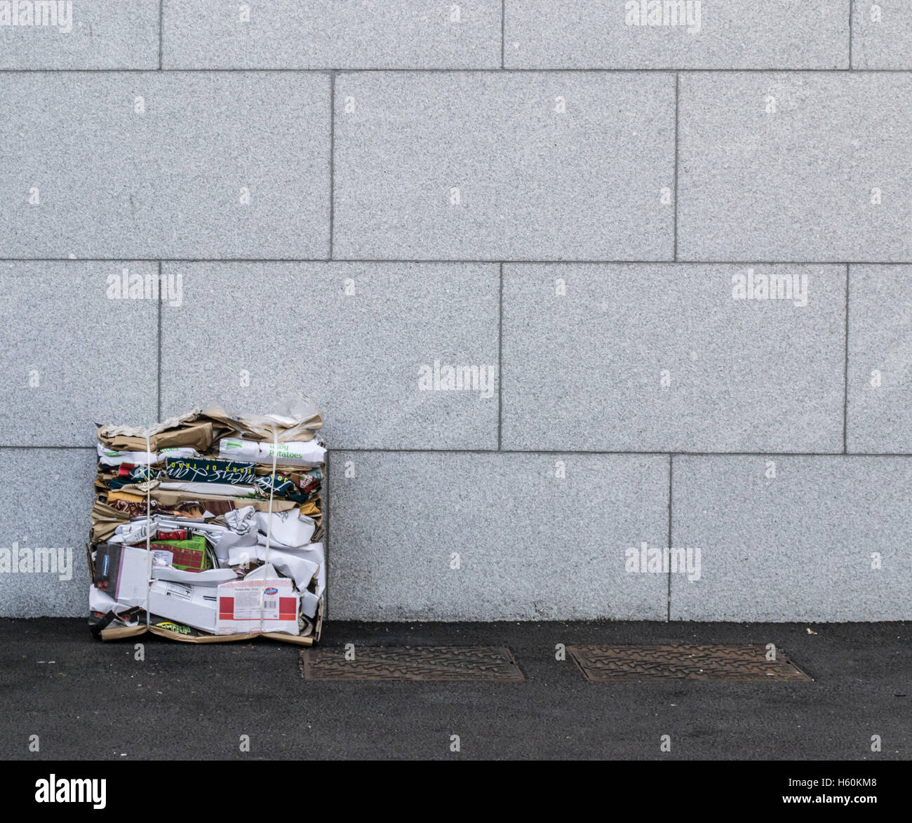 Appiattite la carta e il cartone del riciclaggio si siede contro il grigio di un muro di pietra con i coperchi di scarico sul percorso Foto Stock