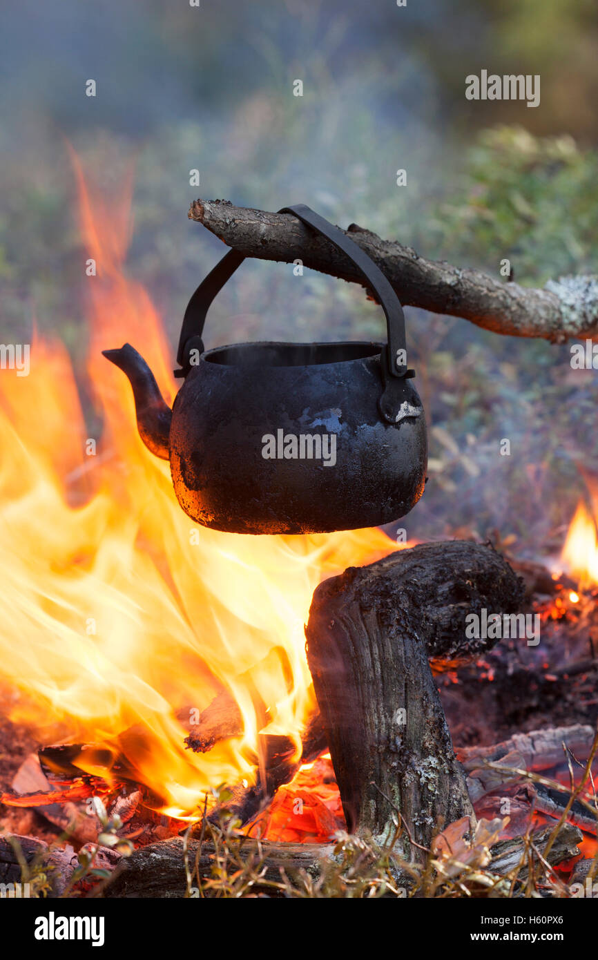 Stagno annerito bollitore dalla fuliggine acqua bollente su fiamme dal fuoco durante il trekking nella foresta Foto Stock