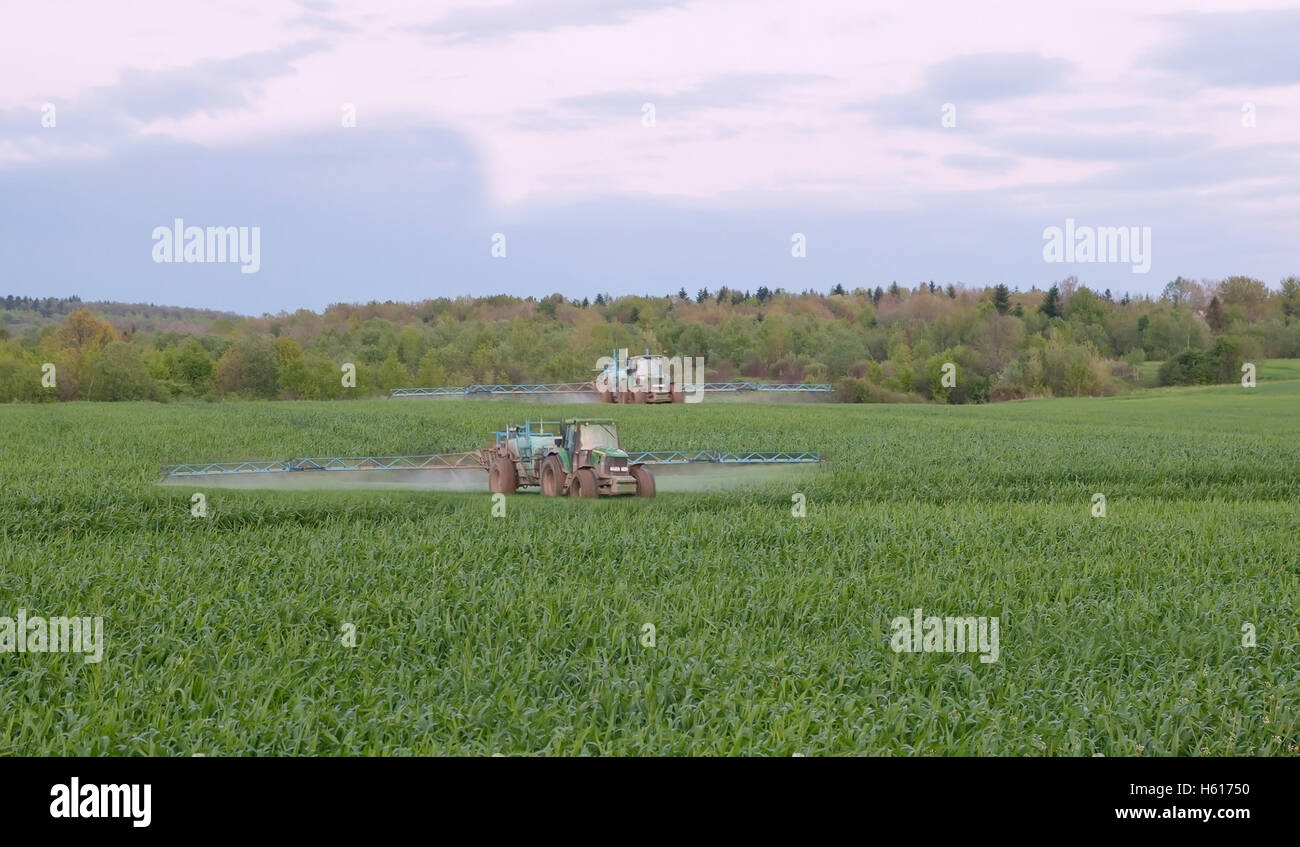 Due trattori la spruzzatura di un campo verde in agriturismo Foto Stock
