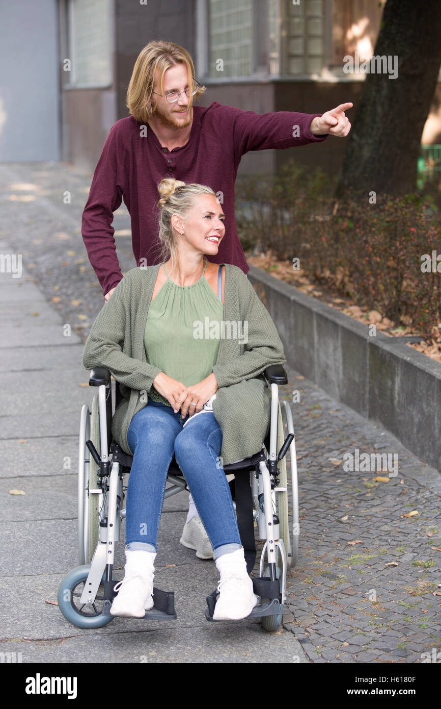 La donna in sedia a rotelle sul marciapiede e giovane uomo che mostra il suo qualcosa Foto Stock