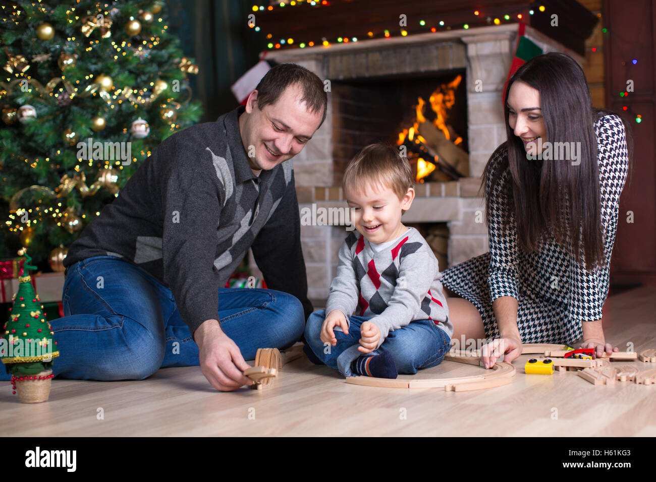 Genitori felici con il loro figlio giocare con modello ferroviario nei pressi di albero di natale in camera Foto Stock