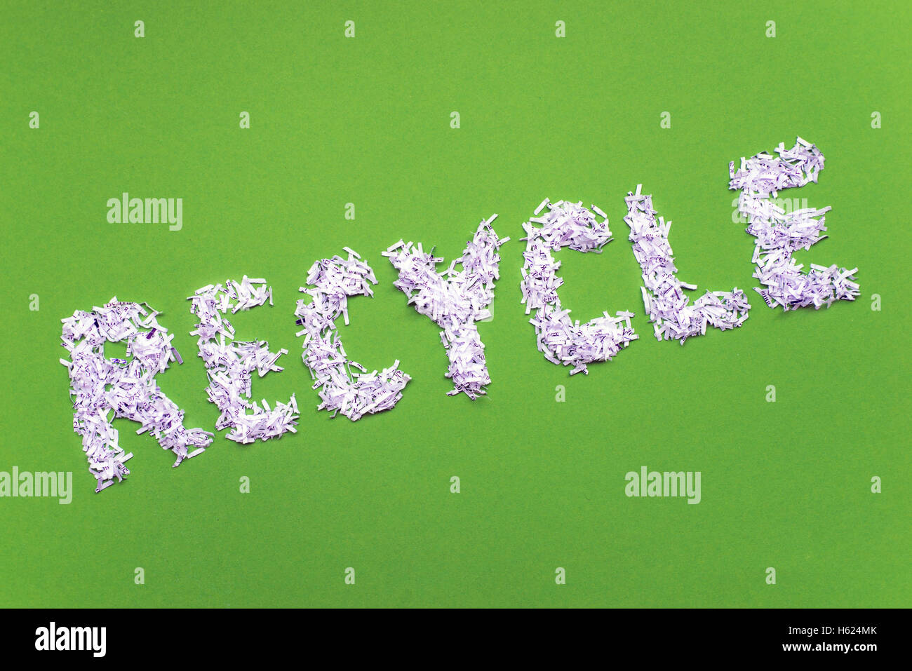 Riciclo inclinato parola fatta dal mucchio di shredded carta bianca brillante su sfondo verde Foto Stock