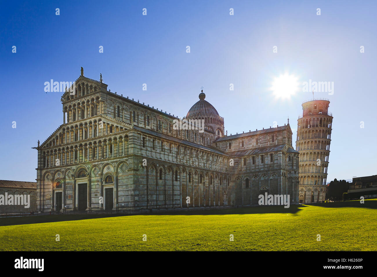 Cattedrale di Pisa con la torre campanaria che è appoggiata contro il Rising Sun. Famoso punto di riferimento italiano su un prato verde di arco della cattedrale Foto Stock