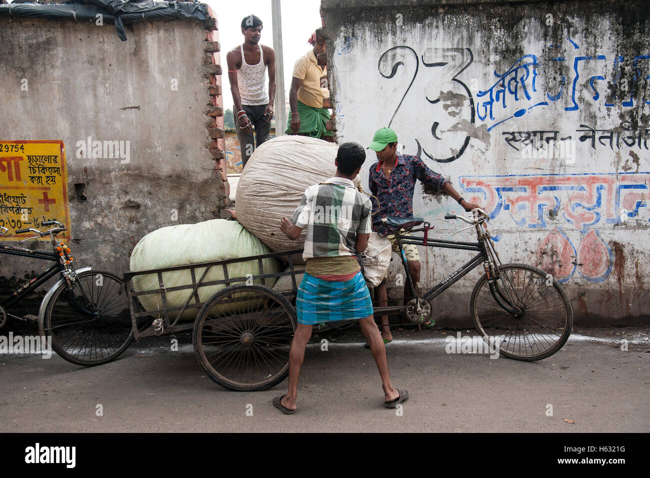 Uomo di tre pacchi di sollevamento sul risciò ciclo vicino stazione ferroviaria Kolkata Foto Stock