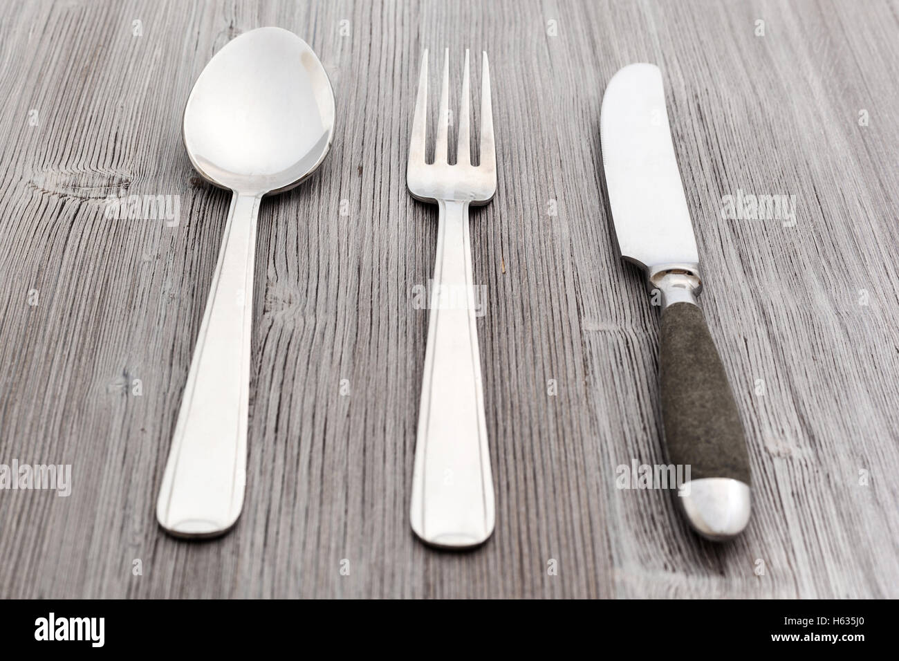 Concetto di cibo - set di posate da tavola coltello, forchetta, cucchiaio per minestra sul marrone chiaro pannello di legno Foto Stock