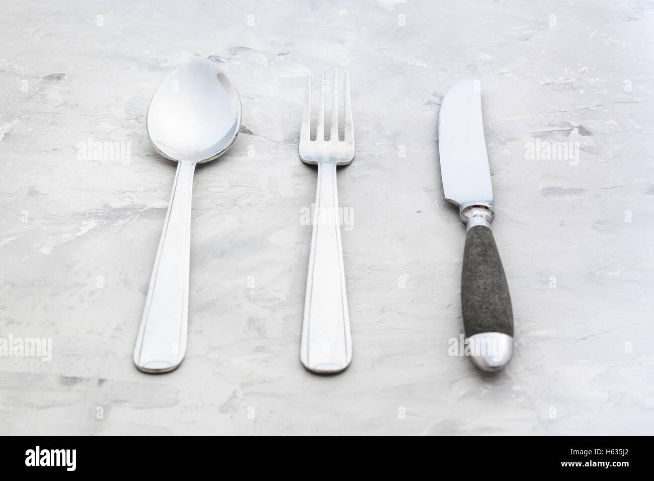Concetto di cibo - set di posate da tavola coltello, forchetta, cucchiaio Zuppa su una superficie in calcestruzzo Foto Stock