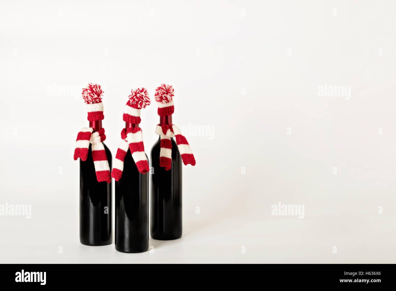 Buon Natale e felice anno nuovo. Tre bottiglie di vino in maglia cappelli e sciarpe a strisce rosse e bianche su un backgro bianco Foto Stock