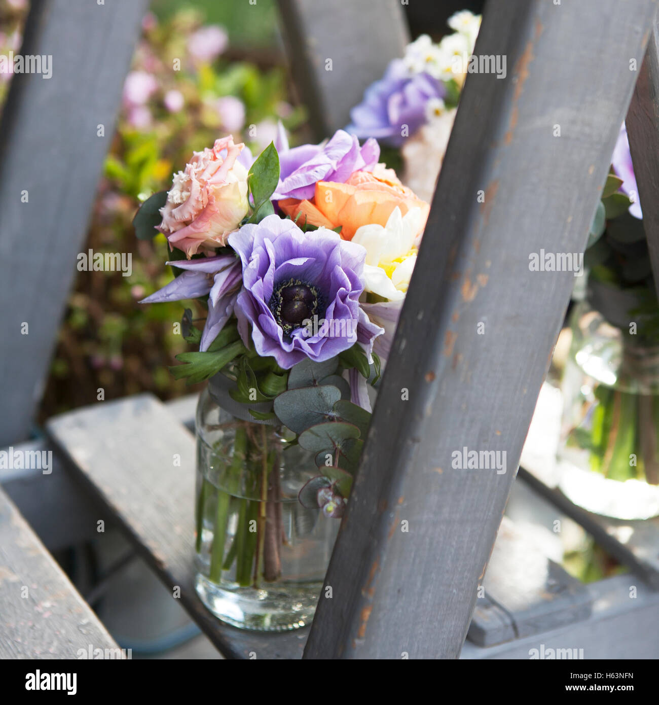 Rose, camomilla, eucalipto, anemone, fresia in un vasetto di vetro sui gradini Foto Stock