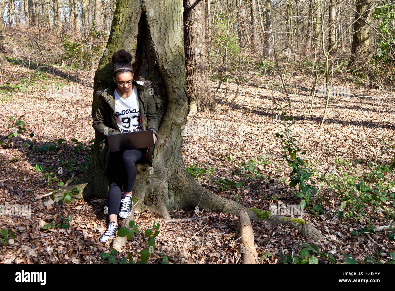 Una razza mista adolescente usando un computer portatile in una radura nel bosco Foto Stock