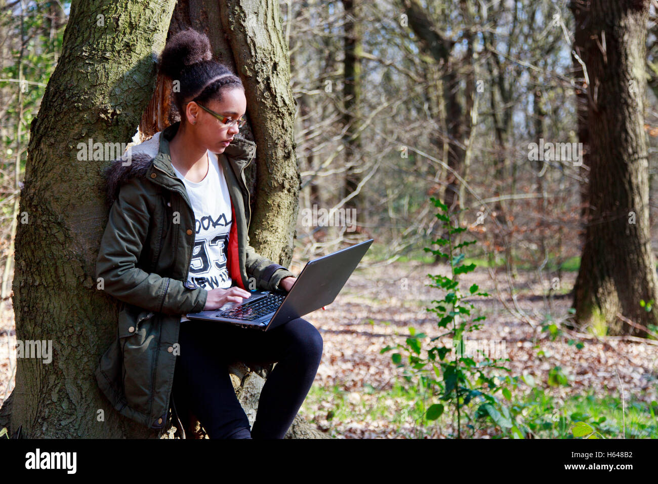 Una razza mista adolescente usando un computer portatile in una radura nel bosco Foto Stock