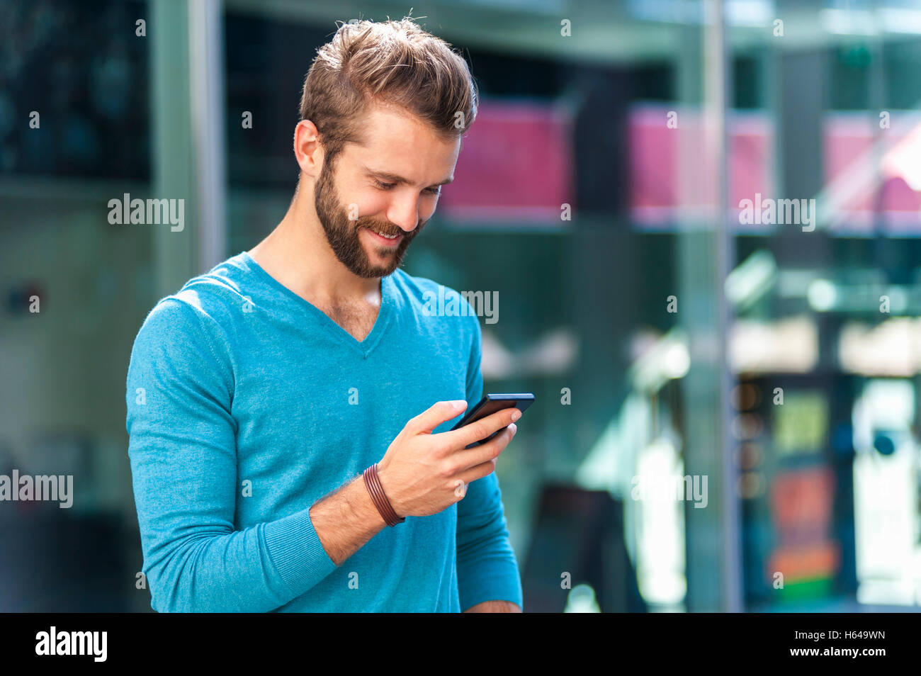Sorridente giovane uomo alla ricerca sul telefono cellulare Foto Stock