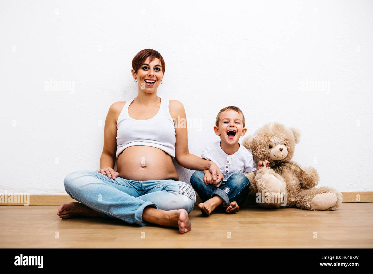 Donna incinta e piccolo figlio seduto sul pavimento ridendo Foto Stock