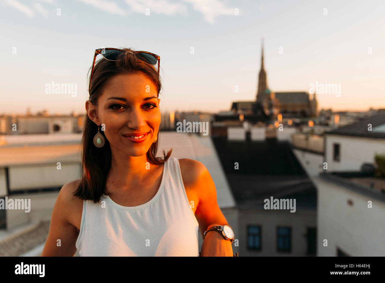 Austria, Vienna, ritratto di sorridere giovane donna sul tetto al tramonto con il Stephansdom in background Foto Stock