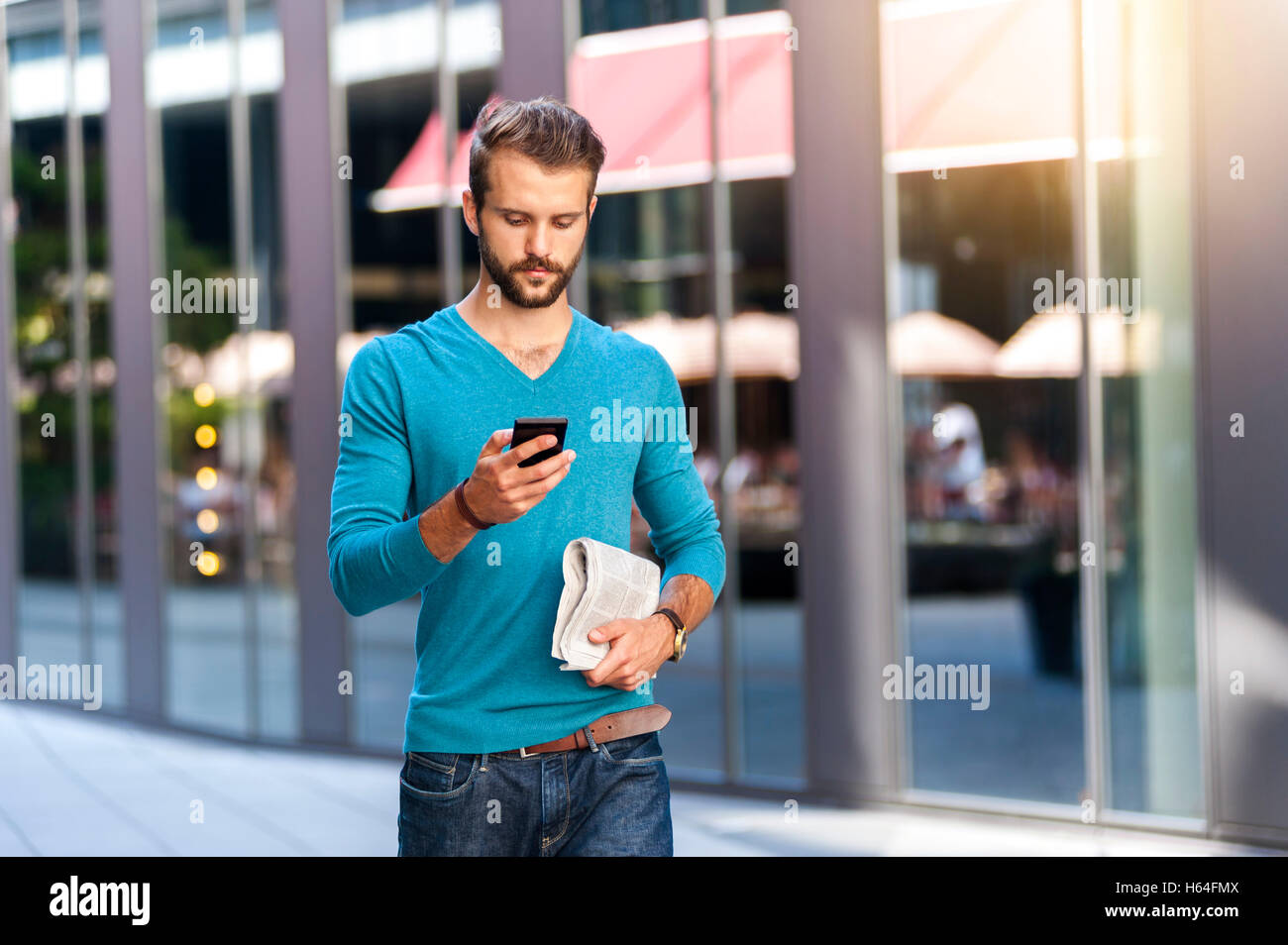Giovane uomo a camminare con un telefono cellulare e il giornale in città Foto Stock
