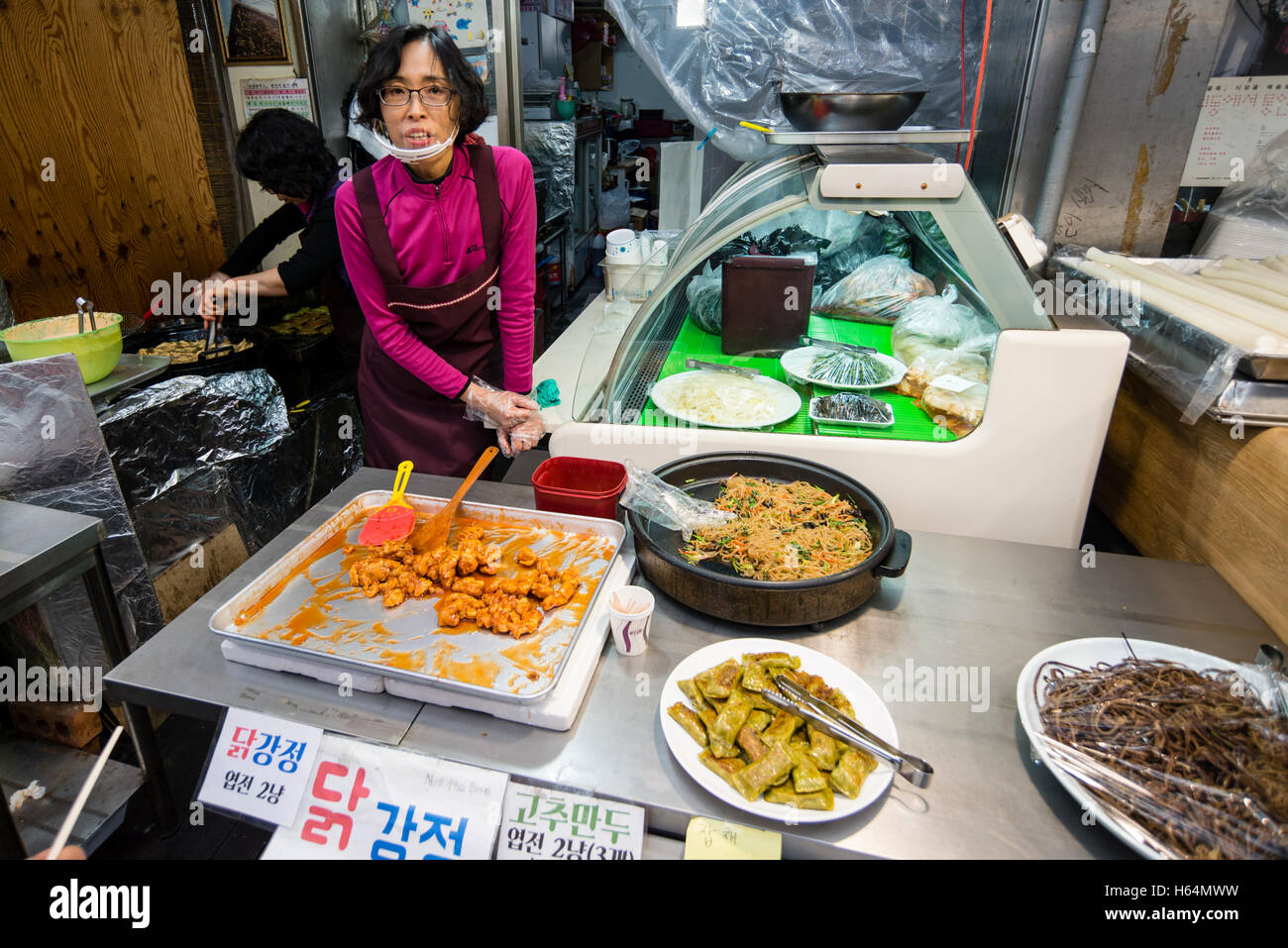 Una femmina di venditore a vendere dakgangjeong (dolce fritto di pollo croccante) a una pressione di stallo alimentare nel mercato Tongin, Jongno-gu, Seoul, Corea Foto Stock