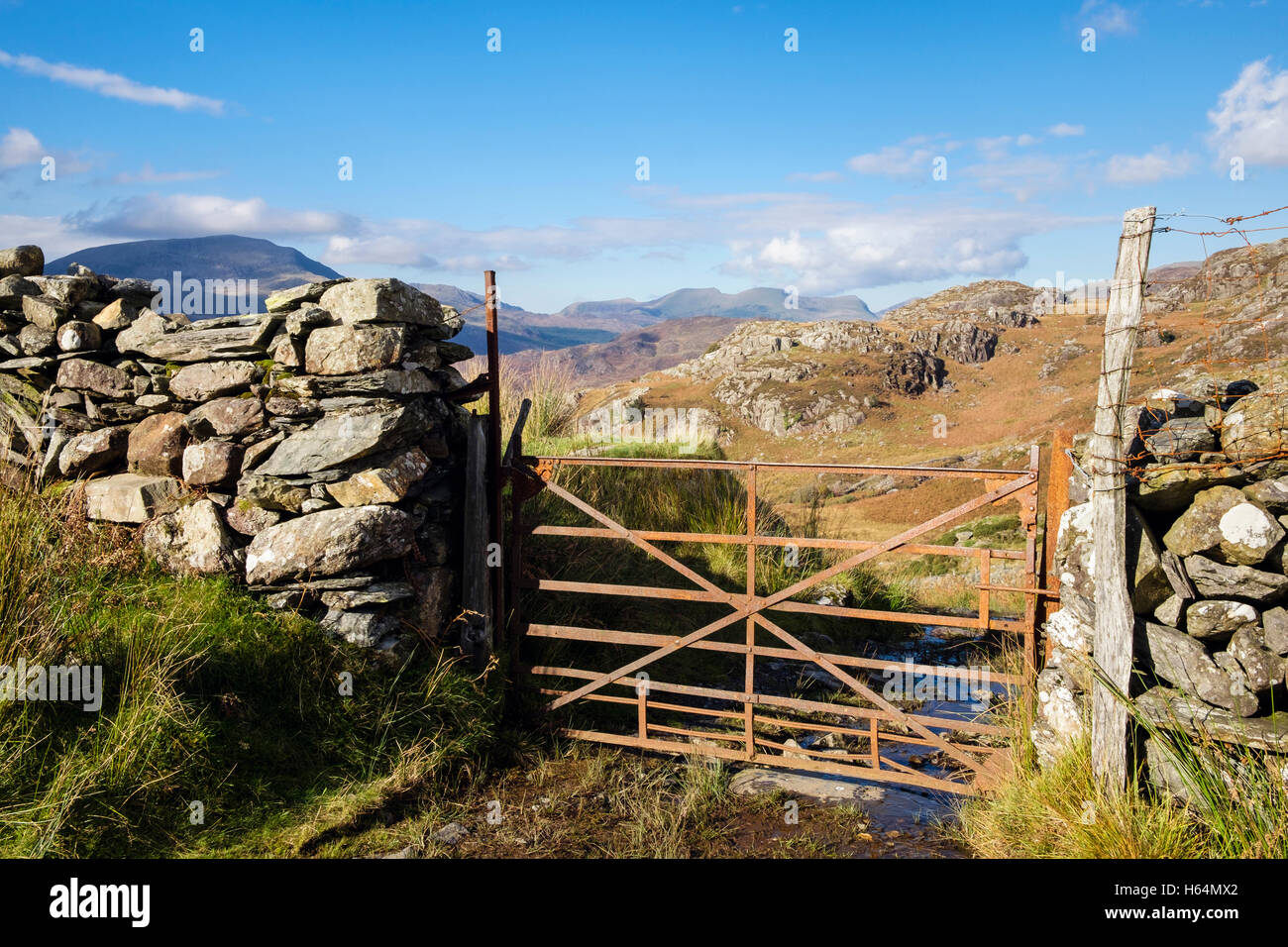 Muro di pietra e rustica fattoria arrugginita cancello su pista di campagna con Nantlle Ridge in lontananza nel Parco Nazionale di Snowdonia (Eryri). Gwynedd Galles del Nord Regno Unito Foto Stock