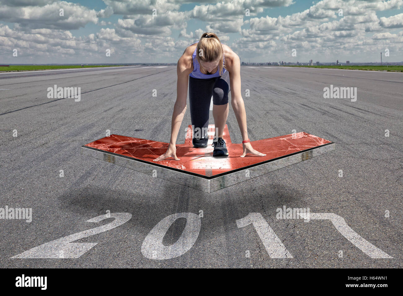 Femminile si inginocchia in posizione di avvio su un galleggiante rosso piattaforma freccia, che è posto al di sopra di una pista di aeroporto superficie. Foto Stock