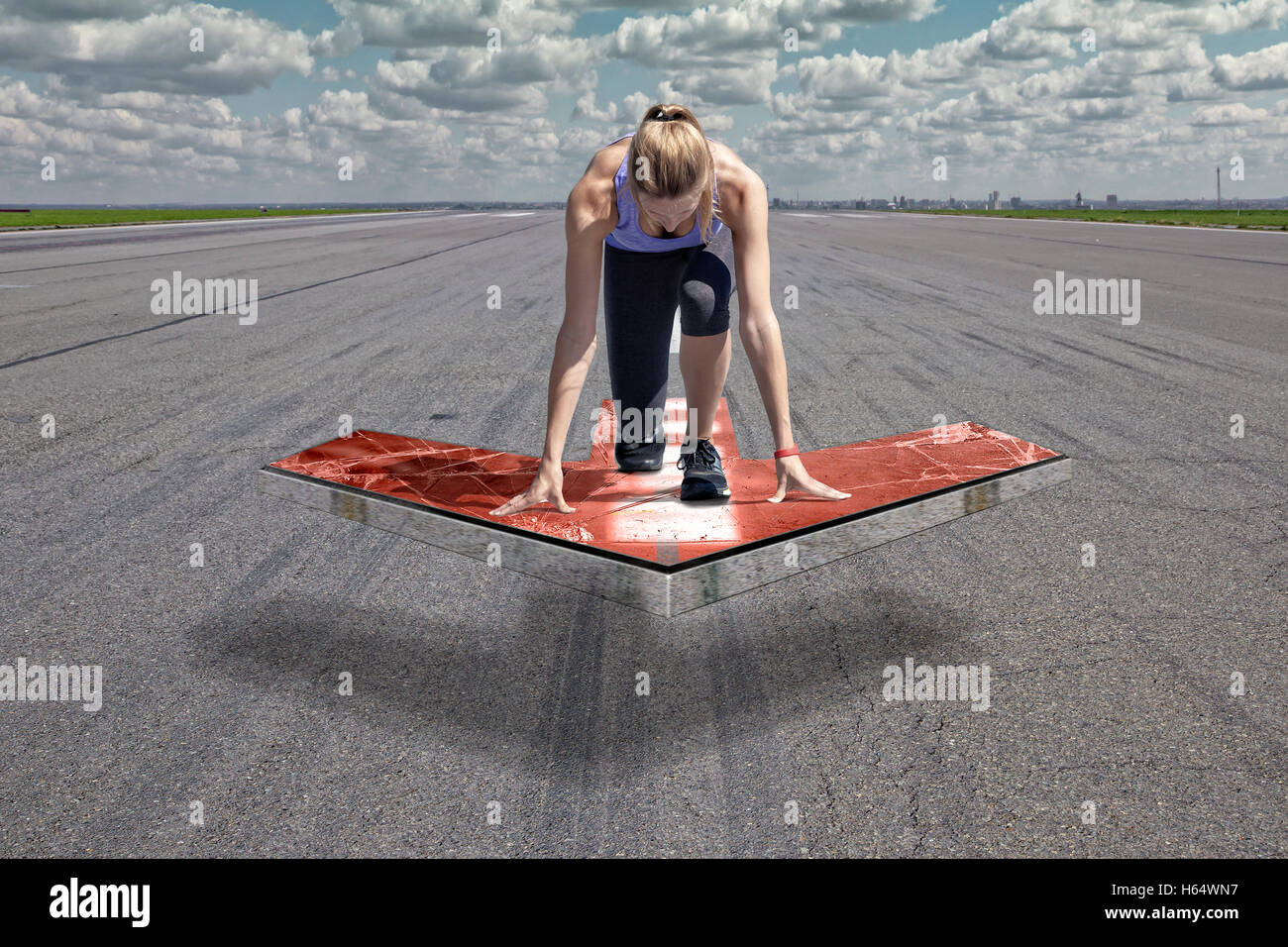 Femminile si inginocchia in posizione di avvio su un galleggiante rosso piattaforma freccia, che è posto al di sopra di una pista di aeroporto superficie. Foto Stock